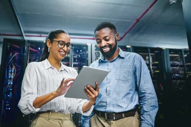 Two smiling colleagues reviewing a tablet in a server room